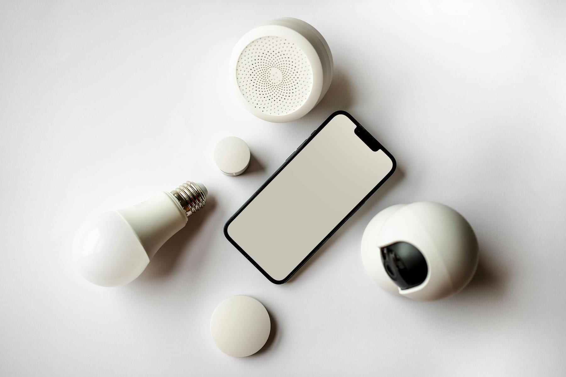Flat lay of smartphone and smart home devices on a white backdrop, showcasing modern technology. on The Tech Shelf
