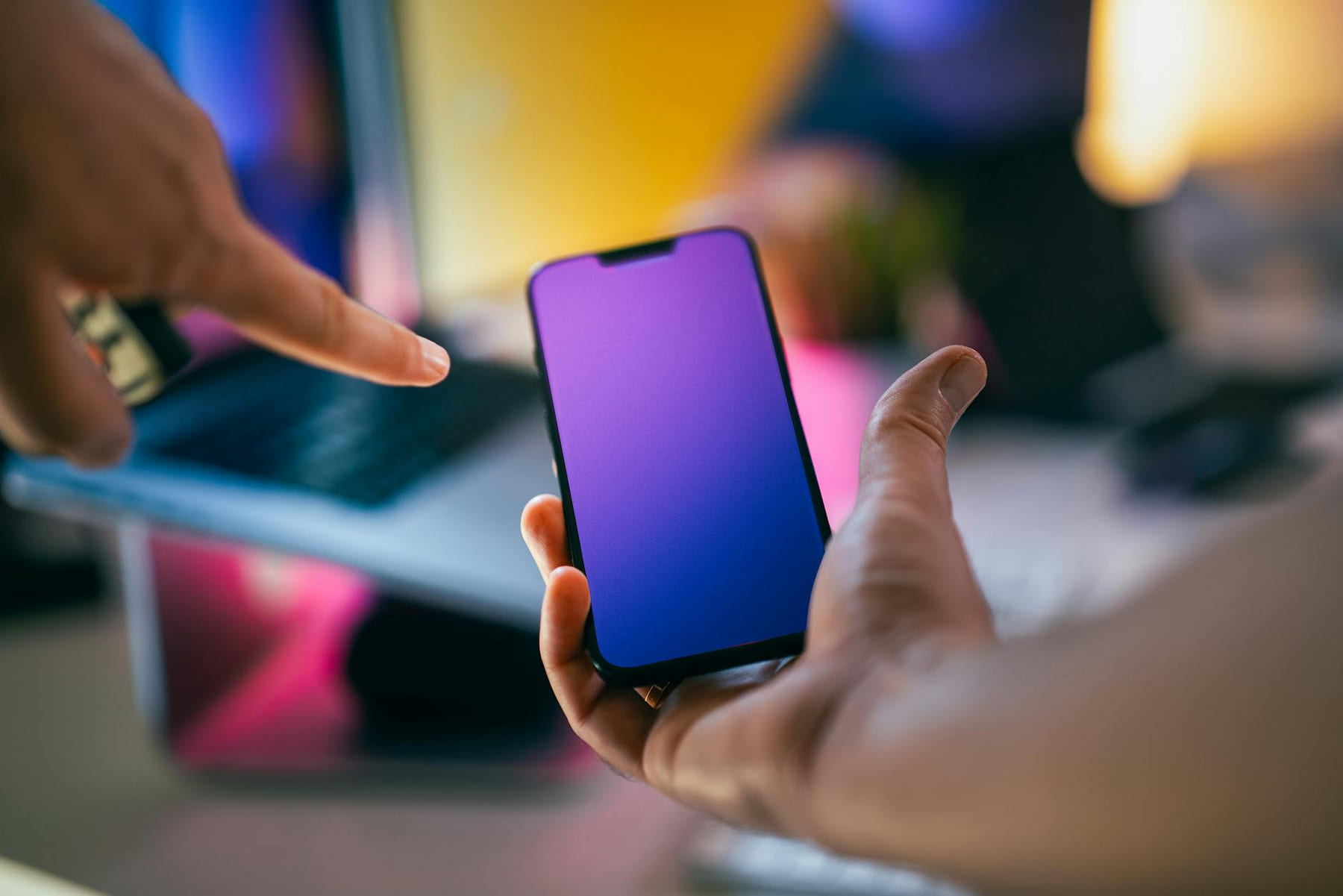 Hands pointing at a smartphone with a gradient screen in an office setting. on The Tech Shelf
