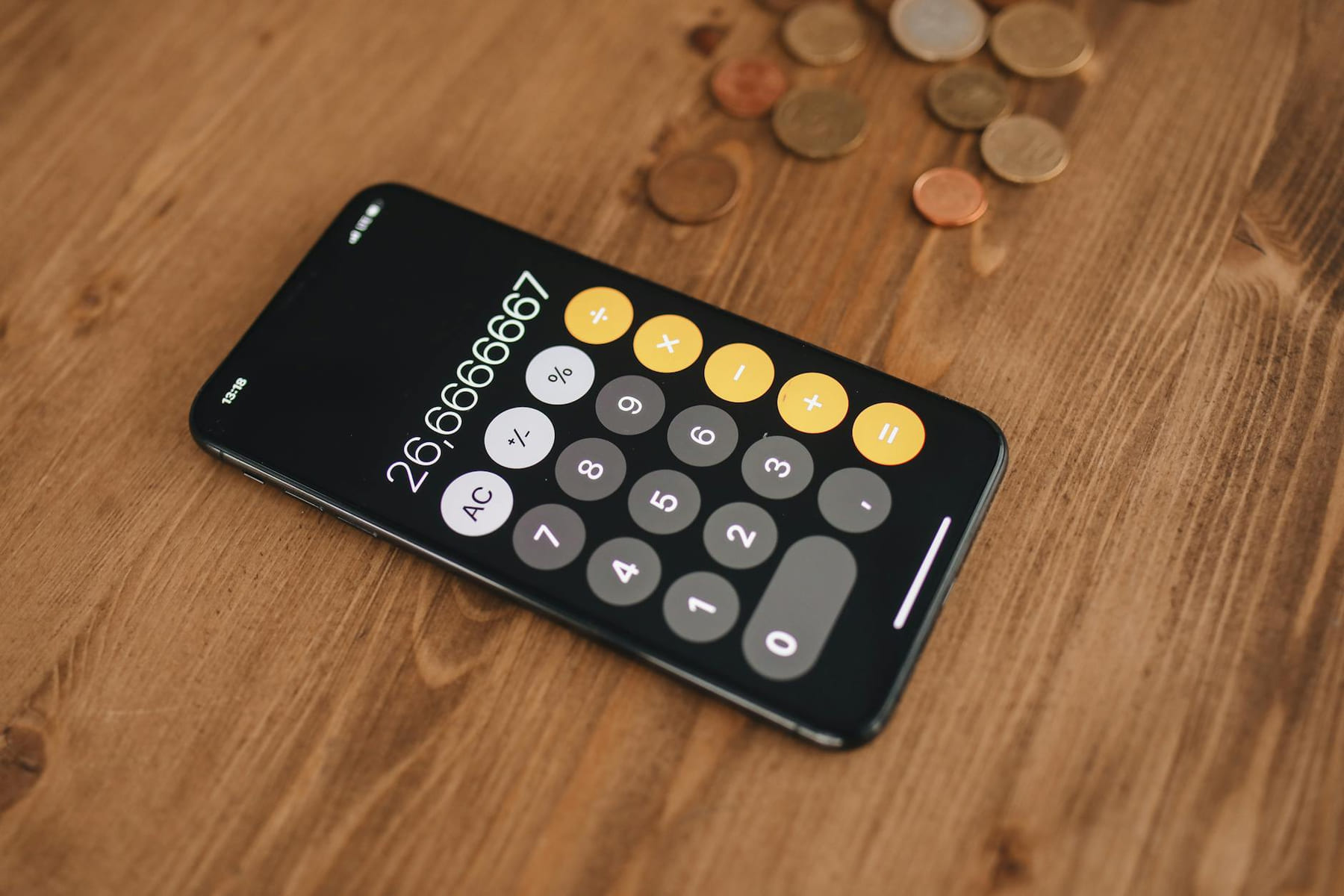 A close-up of a smartphone displaying a calculator app surrounded by coins on a wooden table. on The Tech Shelf