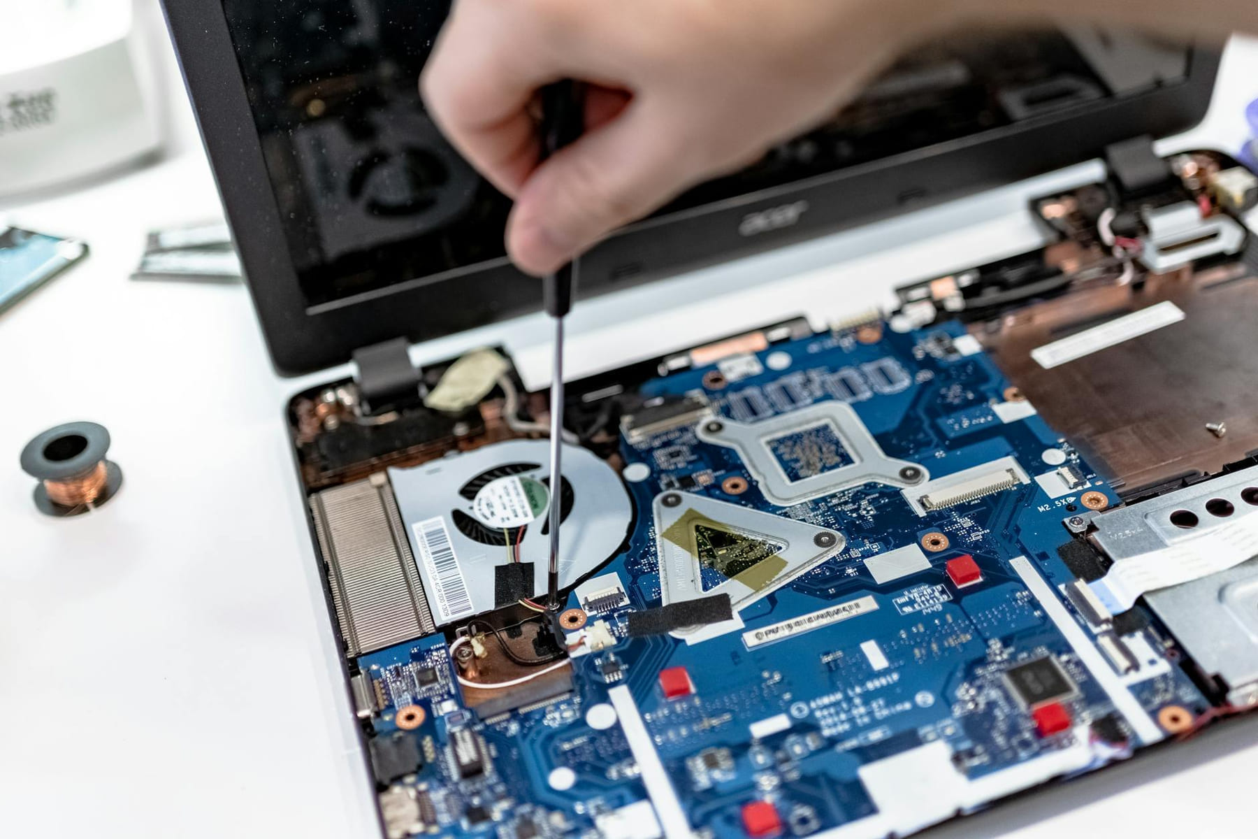 Hand repairing a laptop motherboard with a screwdriver, highlighting tech maintenance. on The Tech Shelf